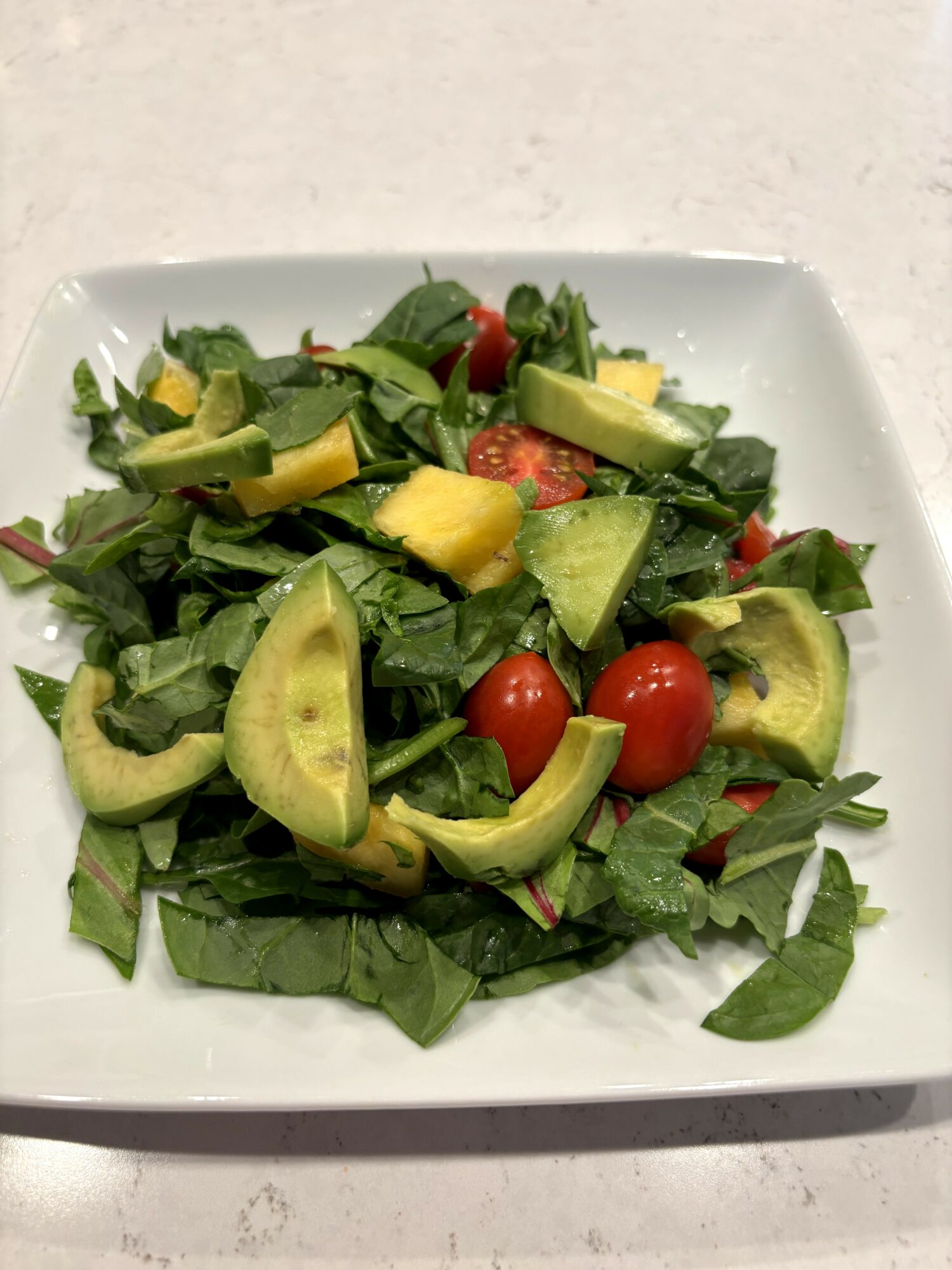 Fresh salad with cherry tomatoes, avocado slices, and leafy greens on a white plate.