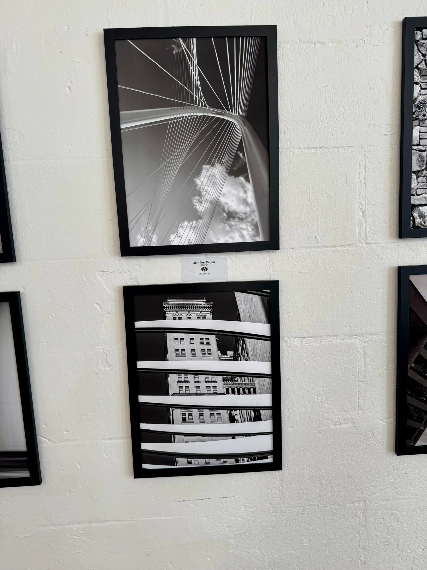 Two framed black and white abstract photographs on a white wall, one above the other, with geometric and architectural patterns.