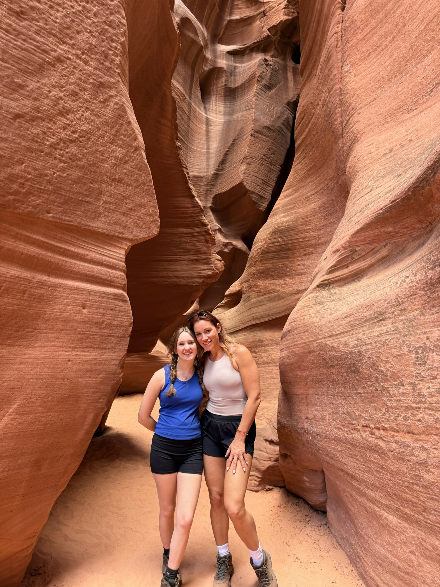 Two women stand close together in a narrow canyon with smooth, layered sandstone walls.