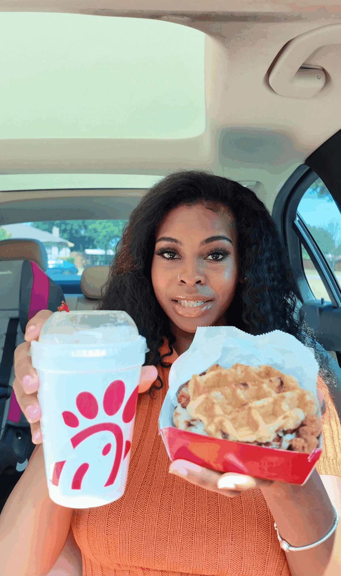 Woman holding a Chick-fil-A drink and a fried chicken sandwich inside a car.