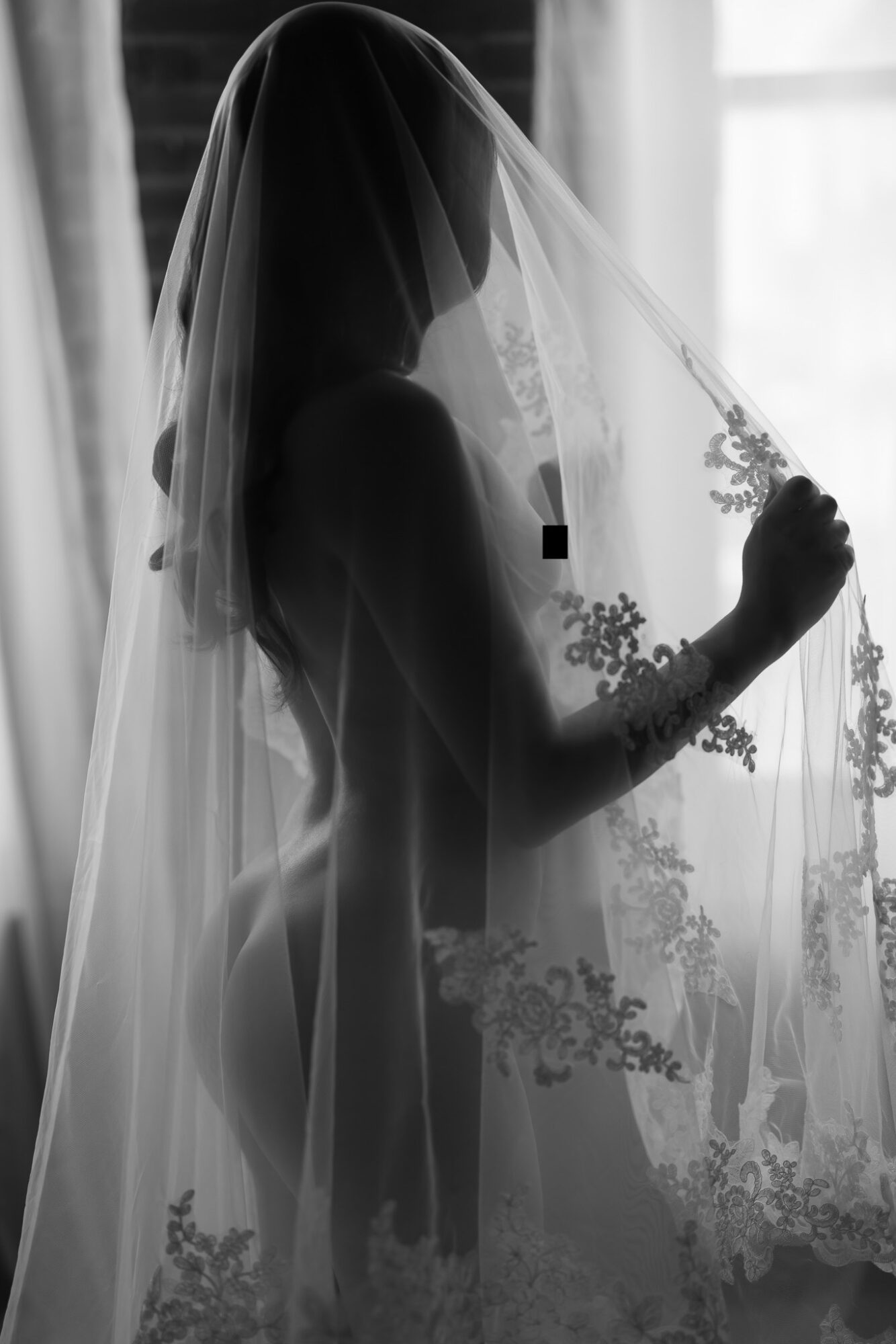 Silhouette of a woman behind a lace curtain, holding the curtain with her hand, backlit by a window.